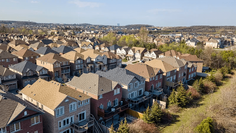Aerial view of a suburban neighborhood with rows of two-story houses, trees, and a clear sky.