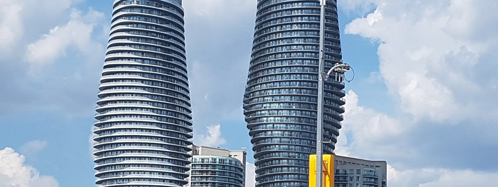 Two modern curved high-rise buildings with glass balconies against a partly cloudy sky.