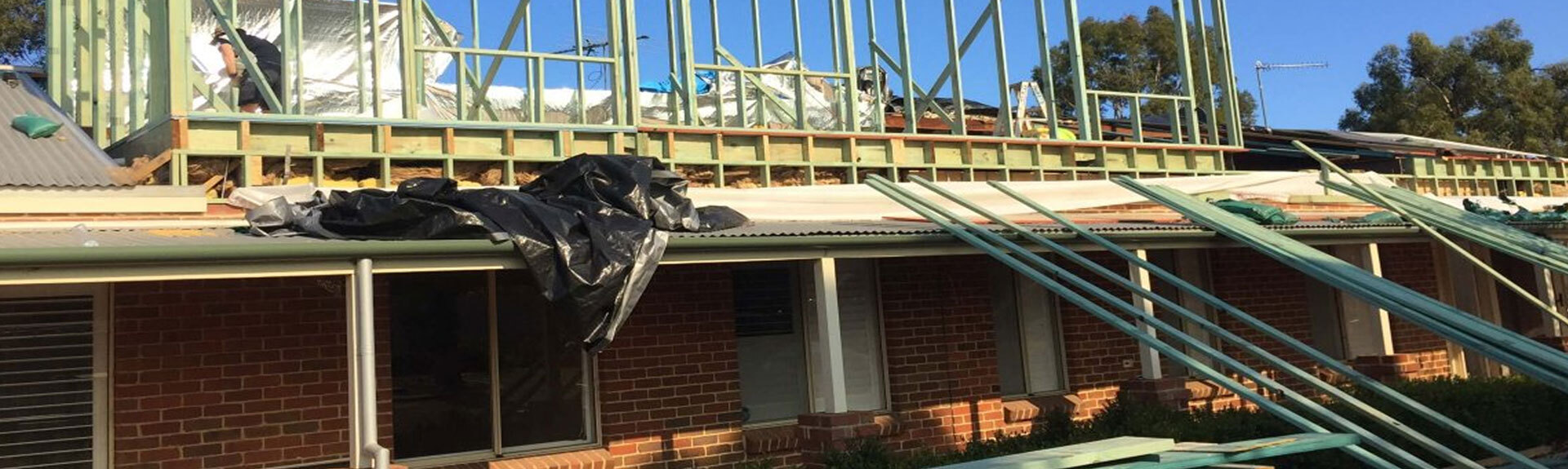 Construction site showing framed wooden structure being added to the second floor of a brick house.