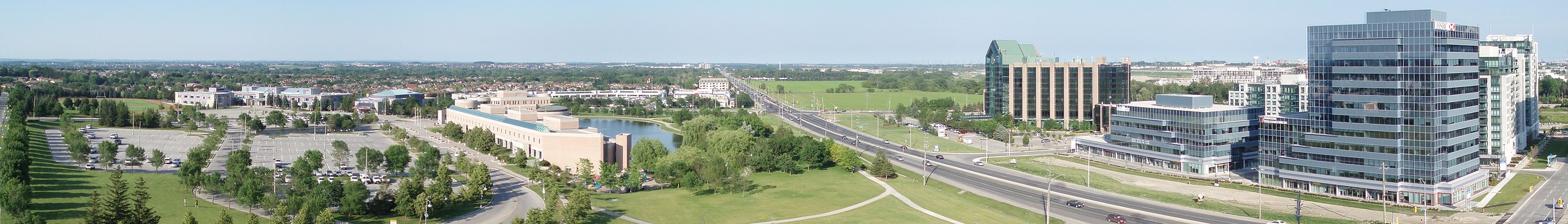 Panoramic view of a suburban area with office buildings, parking lots, green spaces, and a road with moving cars.
