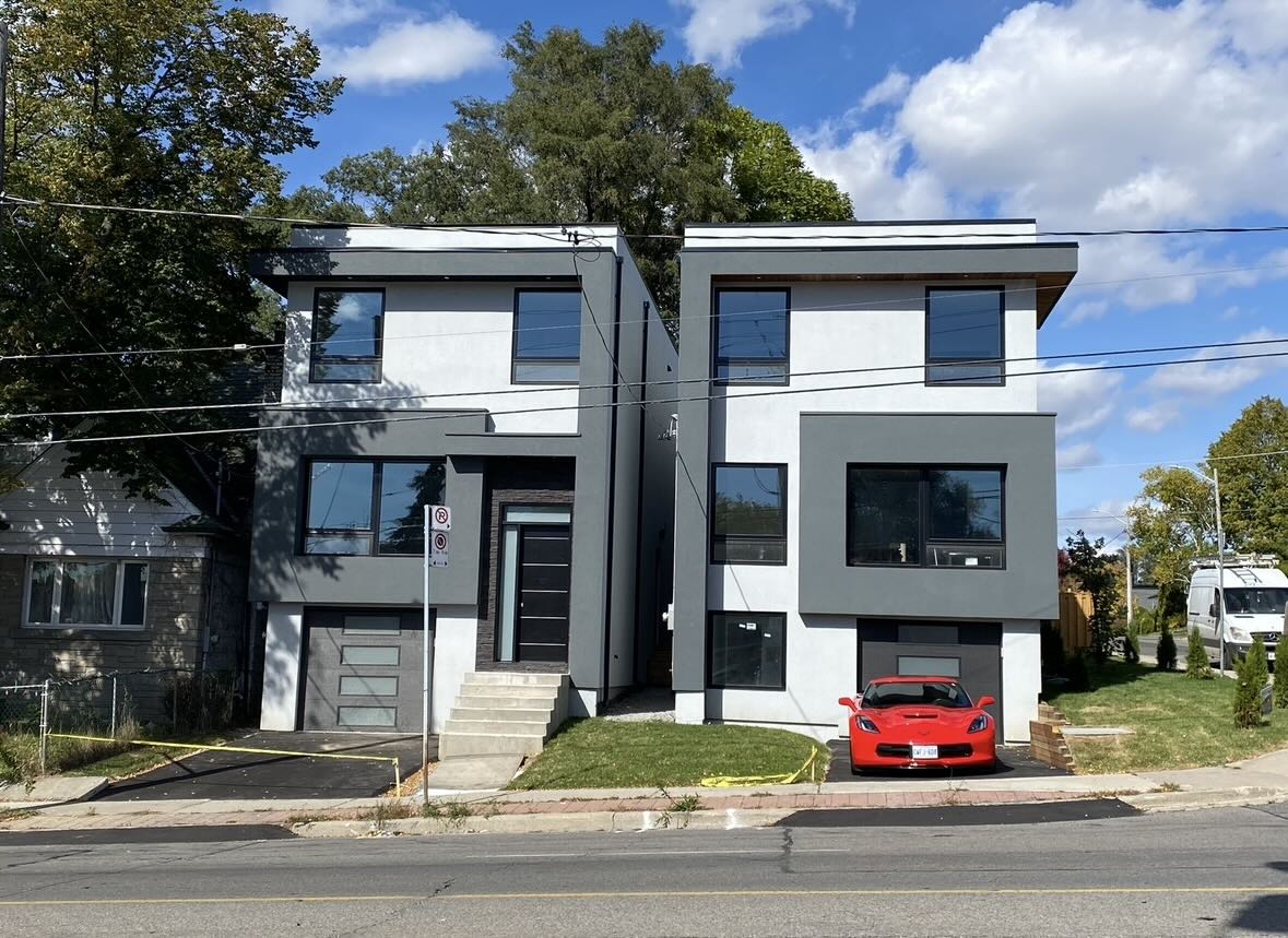 Modern duplex with gray and white exterior, featuring large windows and a red sports car parked in one driveway.