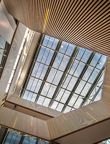 View looking up at a large rectangular glass ceiling framed by wooden slatted walls inside a modern building.